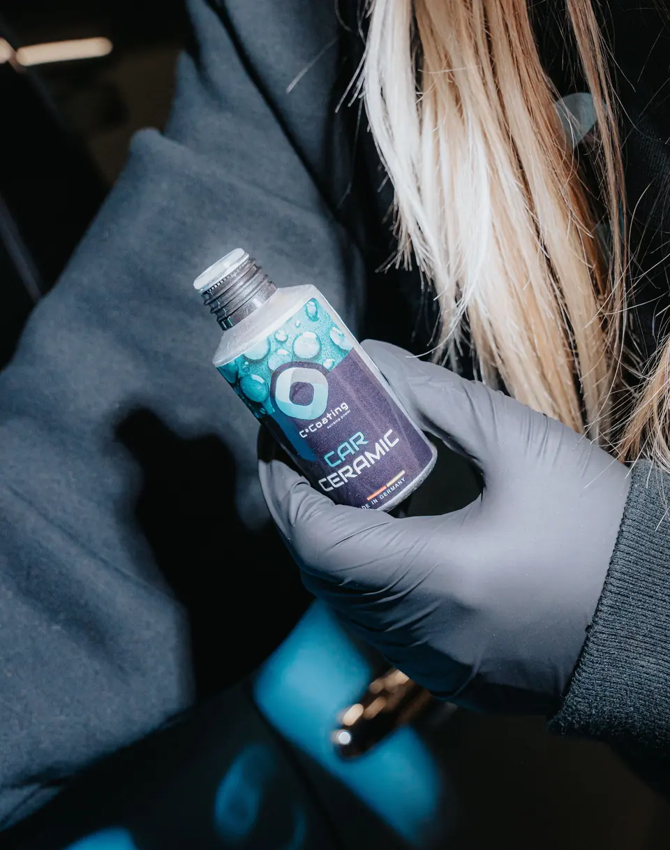 C² Coating Car Ceramic – Flasche der Keramikversiegelung in der Hand vor einem hellblauen Fahrzeug